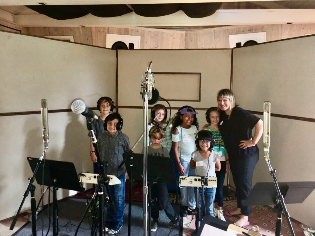 Charissa Nielsen with a children’s choir inside Shangri-La Studios, surrounded by microphones, headphones, and acoustic panels.